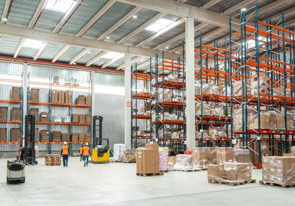 A large warehouse space with racking, shelving, boxes on pallets, and operatives working.