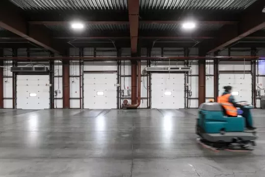 Cleaning operative on a ride-on scrubber dryer speeds across a warehouse floor.